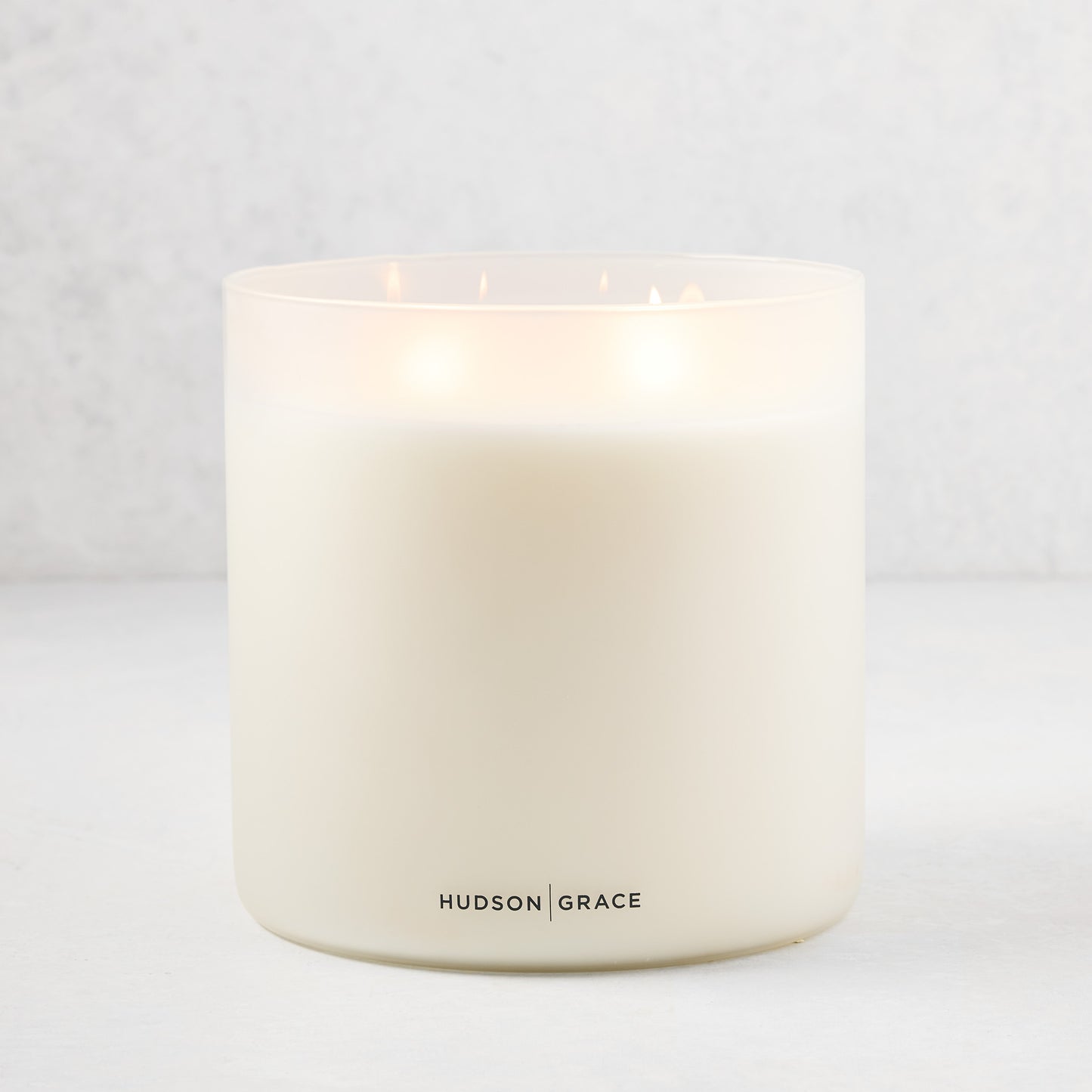 Hudson Grace Original Scented 4-Wick Candle in a white frosted glass vessel, lit.