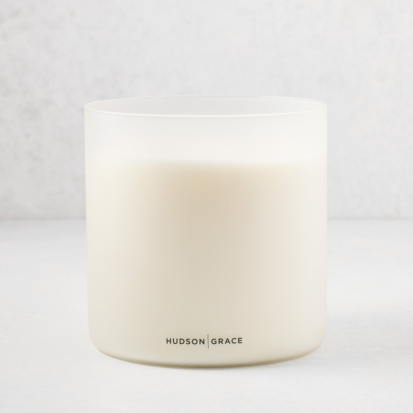 Hudson Grace Original Scented 4-Wick Candle in a frosted white glass vessel with black logo.