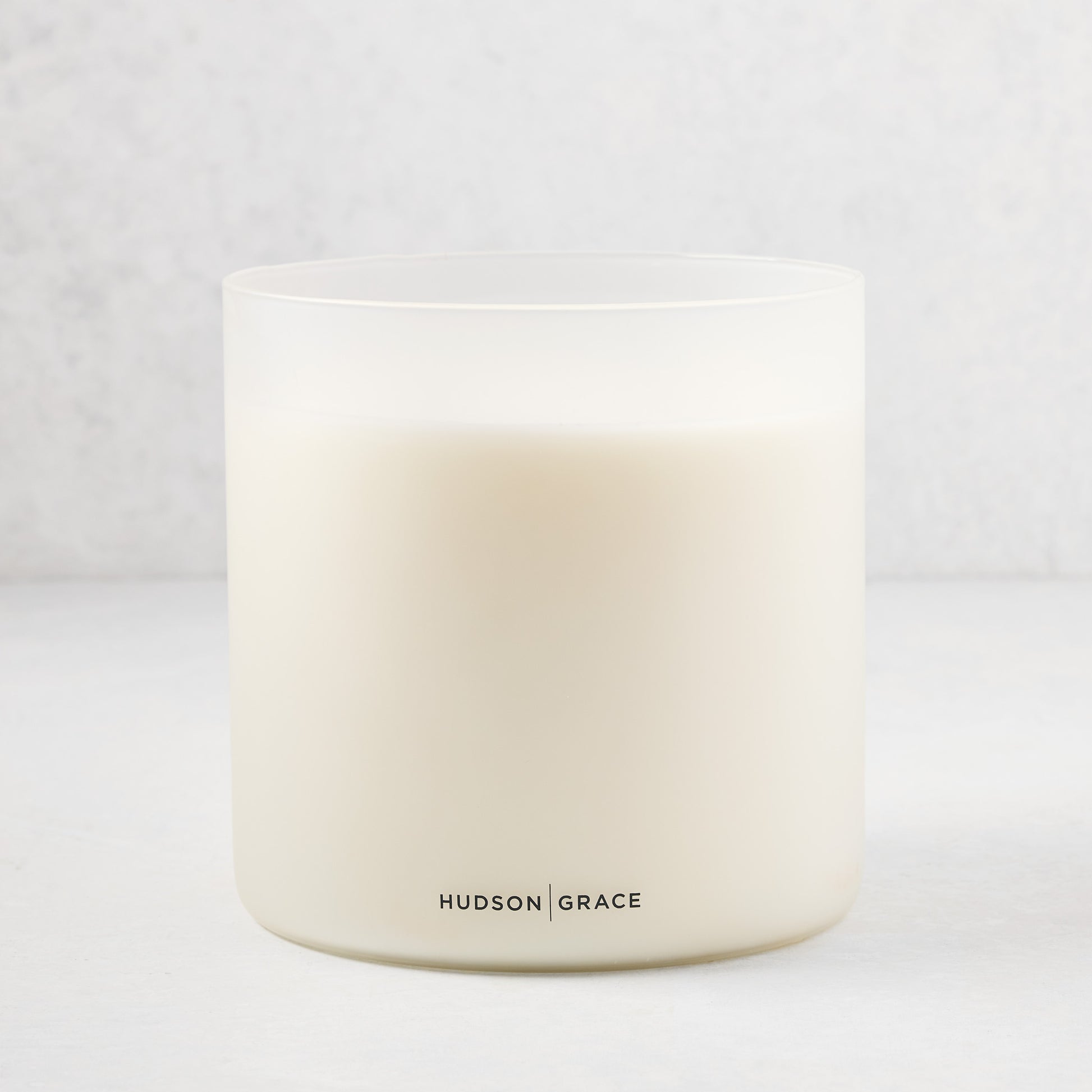 Hudson Grace Original Scented 4-Wick Candle in a frosted white glass vessel with black logo.