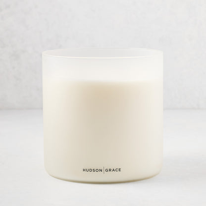 Hudson Grace Original Scented 4-Wick Candle in a frosted white glass vessel with black logo.