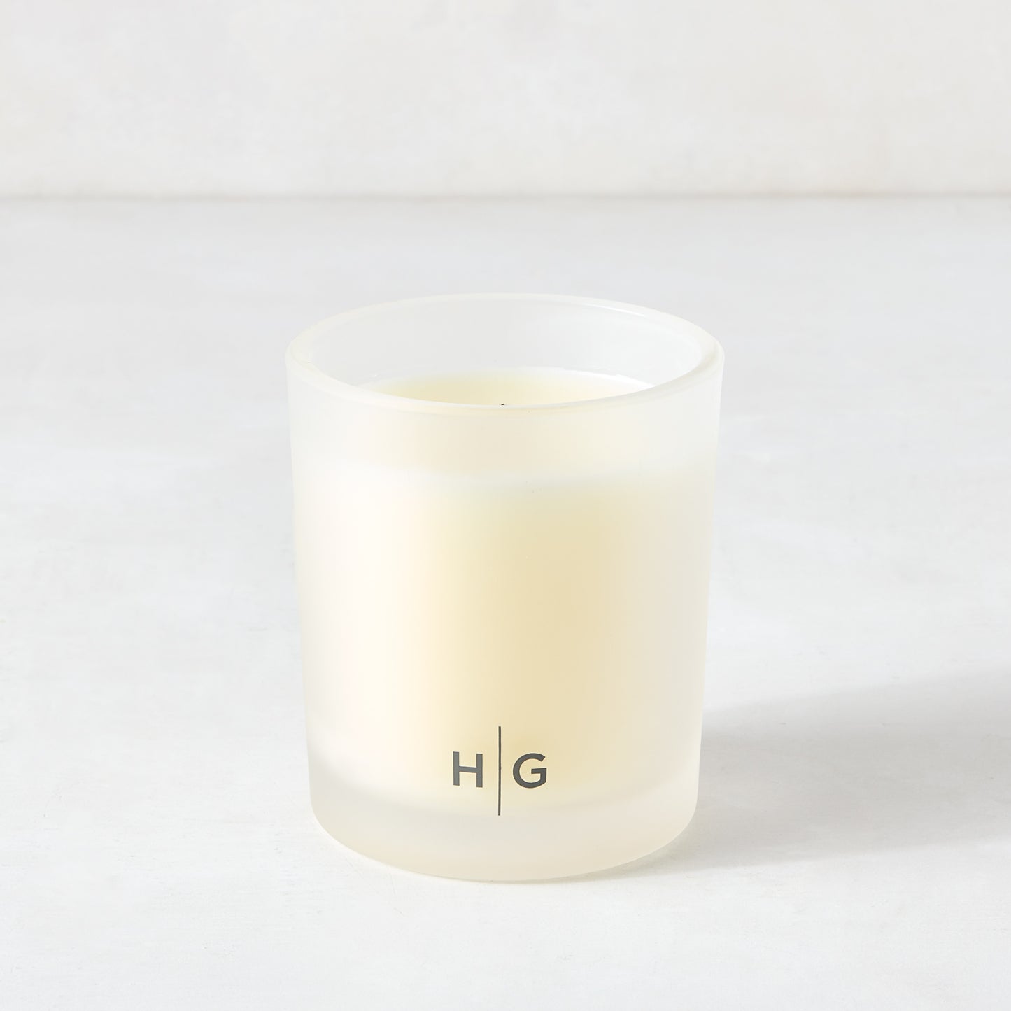 Hudson Grace Original Scented Candle in a frosted glass vessel with "HG" logo, white soy wax.