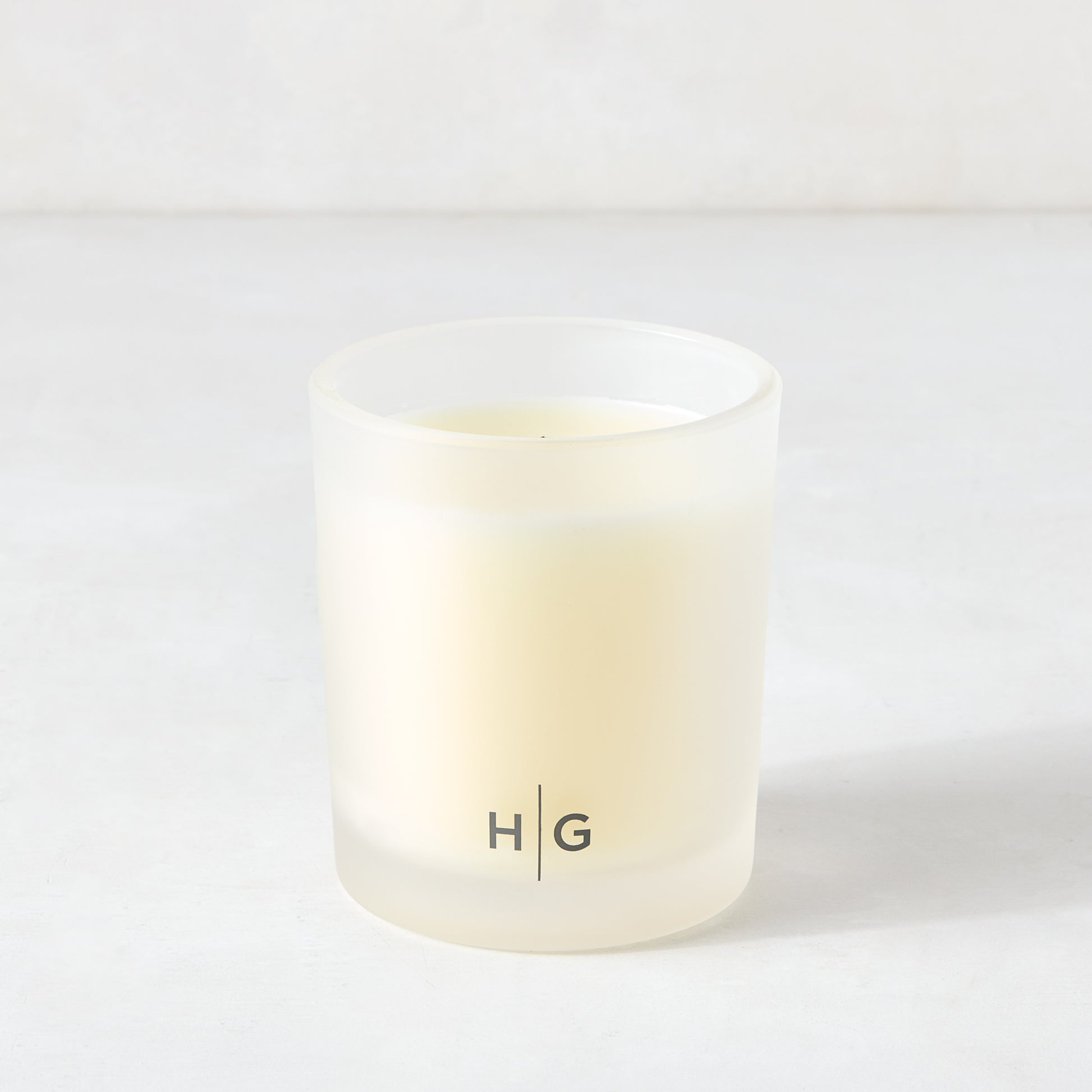 Hudson Grace Original Scented Candle in a frosted glass vessel with "HG" logo, white soy wax.