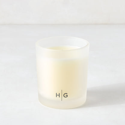 Hudson Grace Original Scented Candle in a frosted glass vessel with "HG" logo, white soy wax.