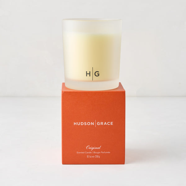 Hudson Grace Original Scented Candle in a frosted glass vessel with "HG" logo, on an orange box.