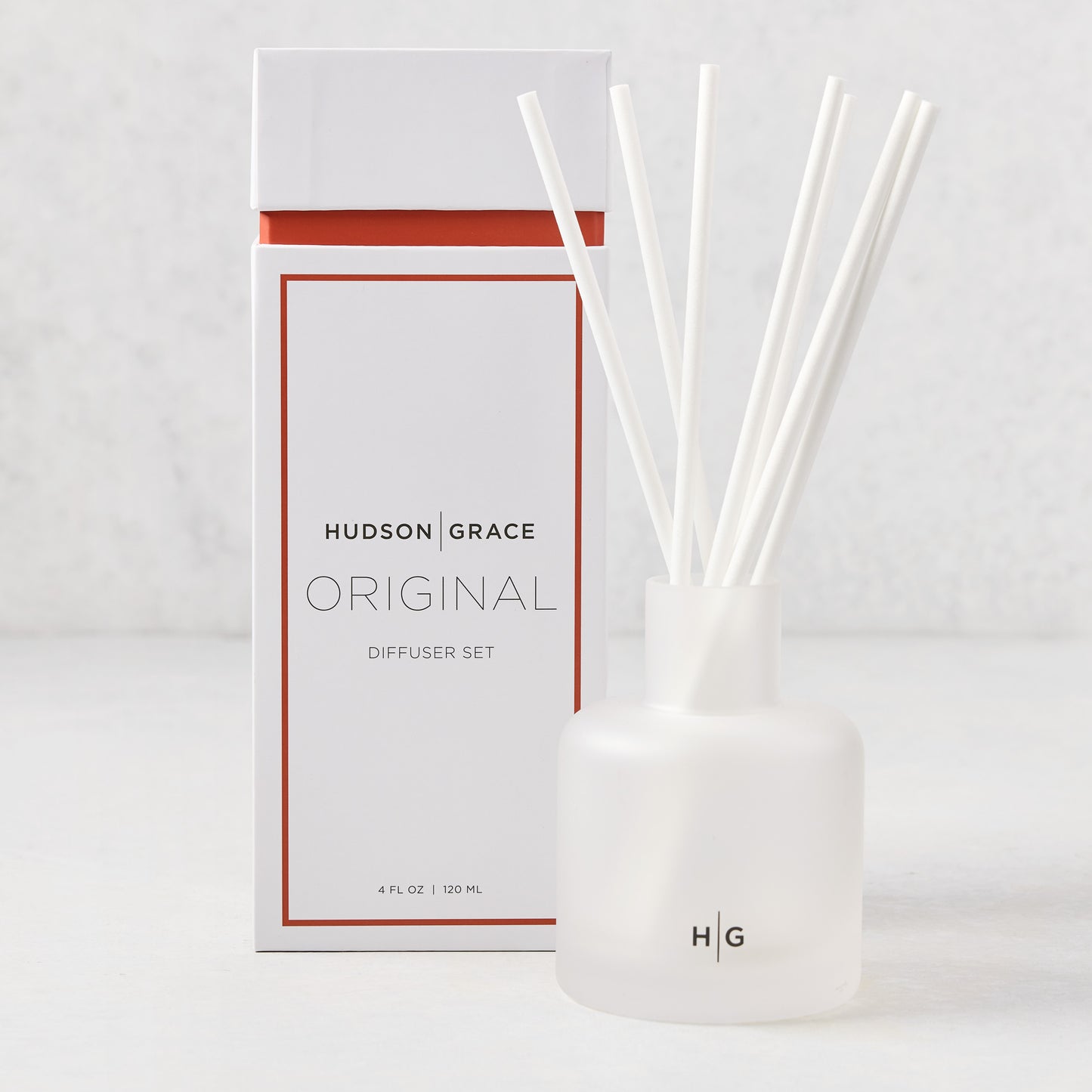 Hudson Grace Original Scented Diffuser set with frosted glass vessel, white reeds, and white box with orange accent.