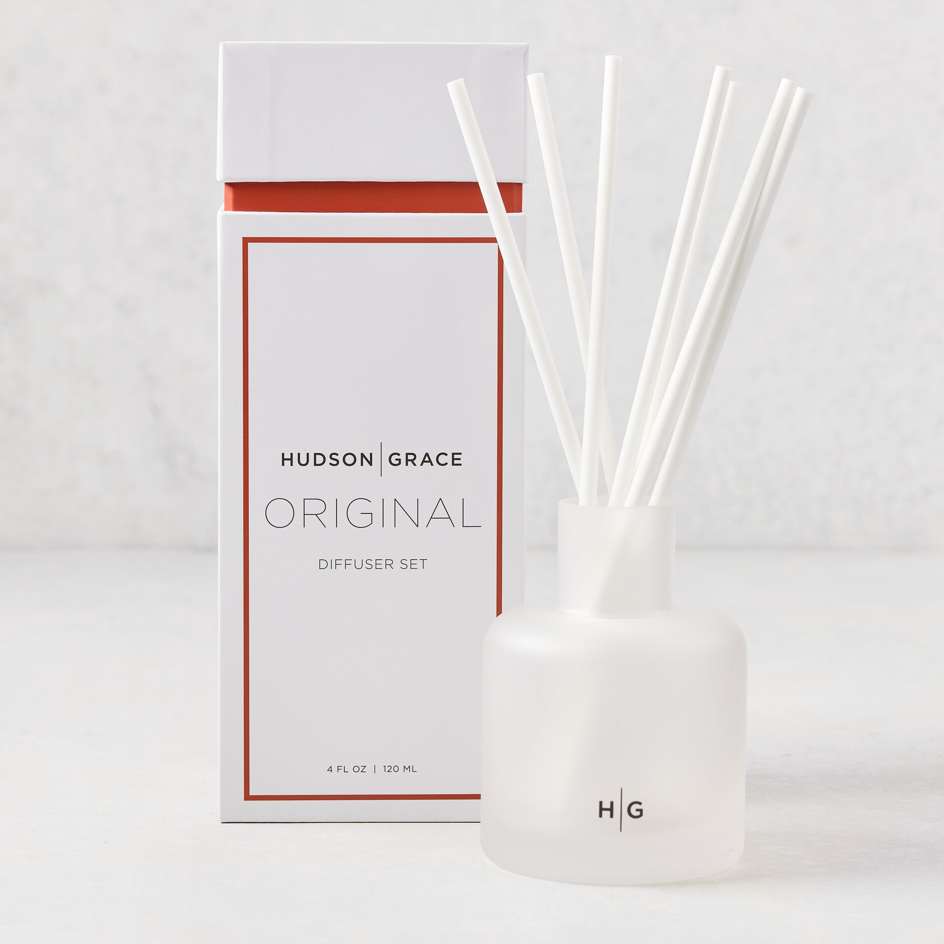 Hudson Grace Original Scented Diffuser set with frosted glass vessel, white reeds, and white box with orange accent.