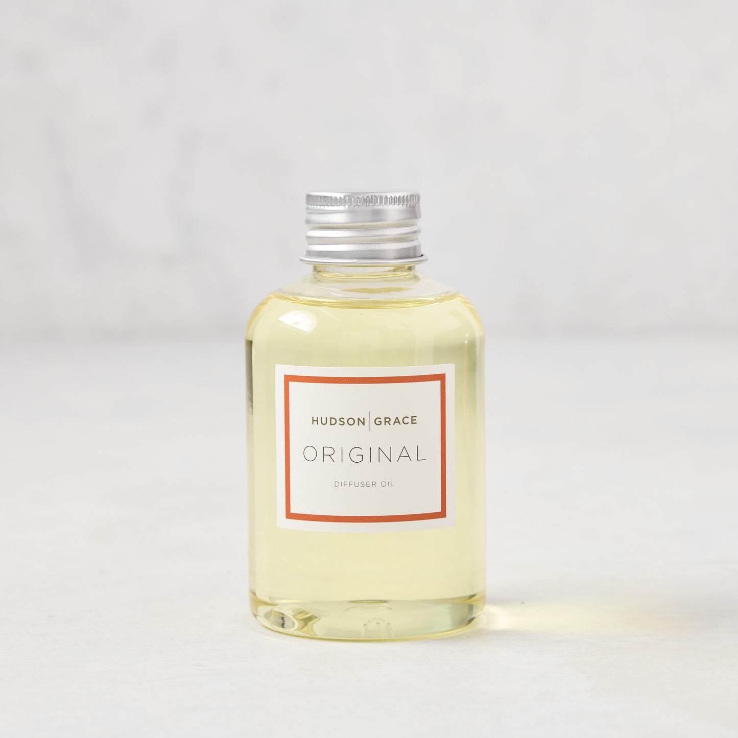 Hudson Grace Original Scented Diffuser Oil, clear glass bottle with silver cap and white label with red border.