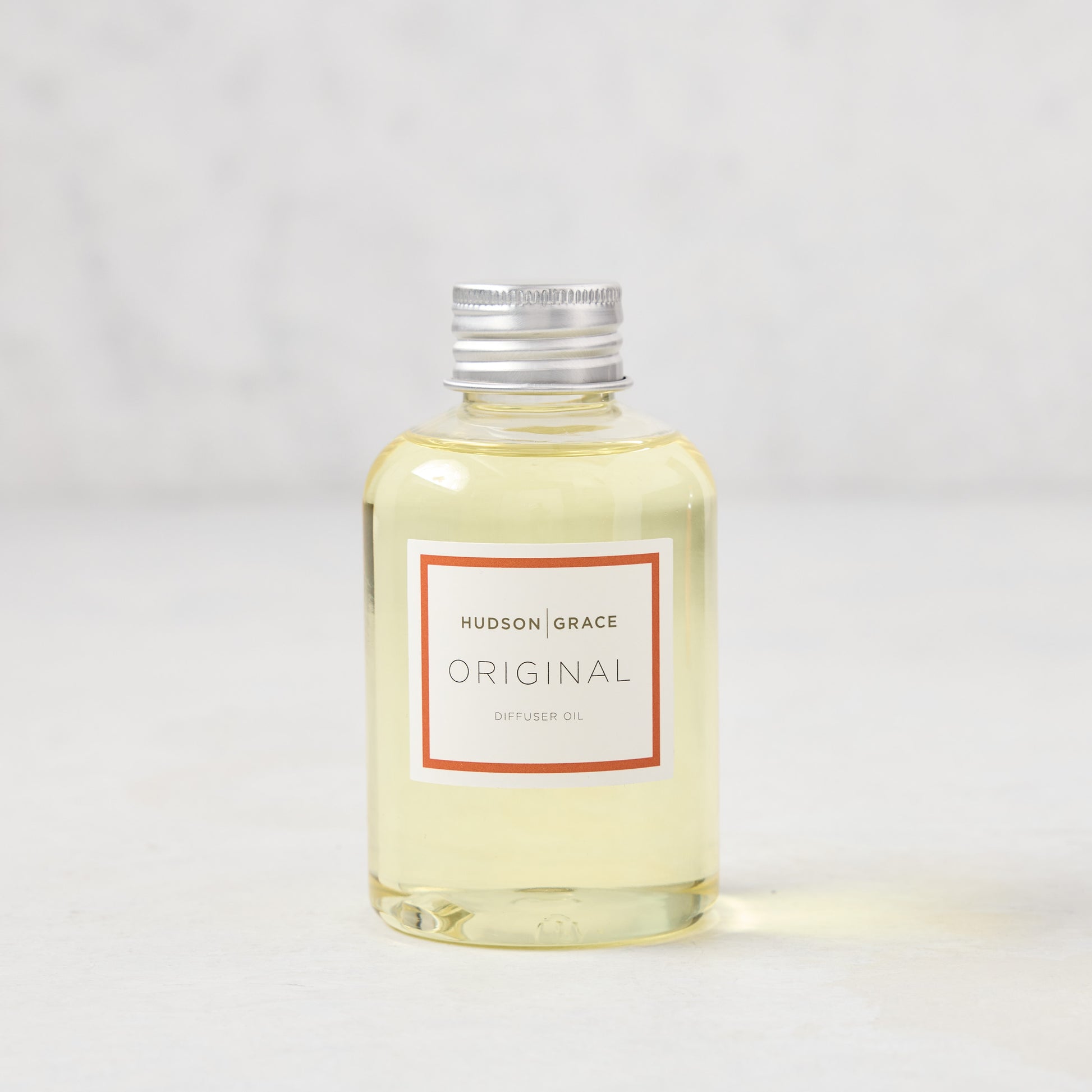 Hudson Grace Original Scented Diffuser Oil, clear glass bottle with silver cap and white label with red border.