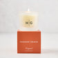 Hudson Grace Original Scented Votive Candle in a frosted glass vessel with HG logo, on an orange gift box.