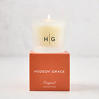 Hudson Grace Original Scented Votive Candle in a frosted glass vessel with HG logo, on an orange gift box.