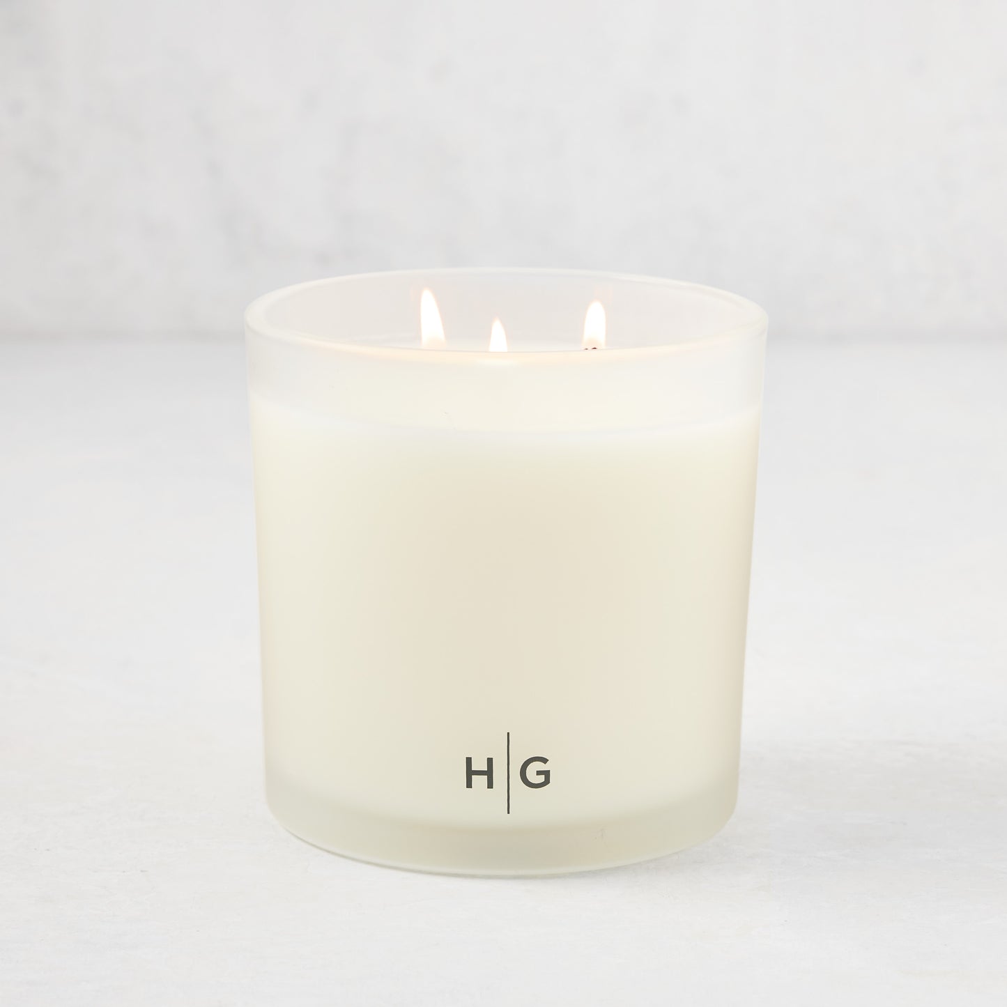 Hudson Grace Palm Beach 3-wick candle in a frosted glass vessel with HG logo, lit wicks.