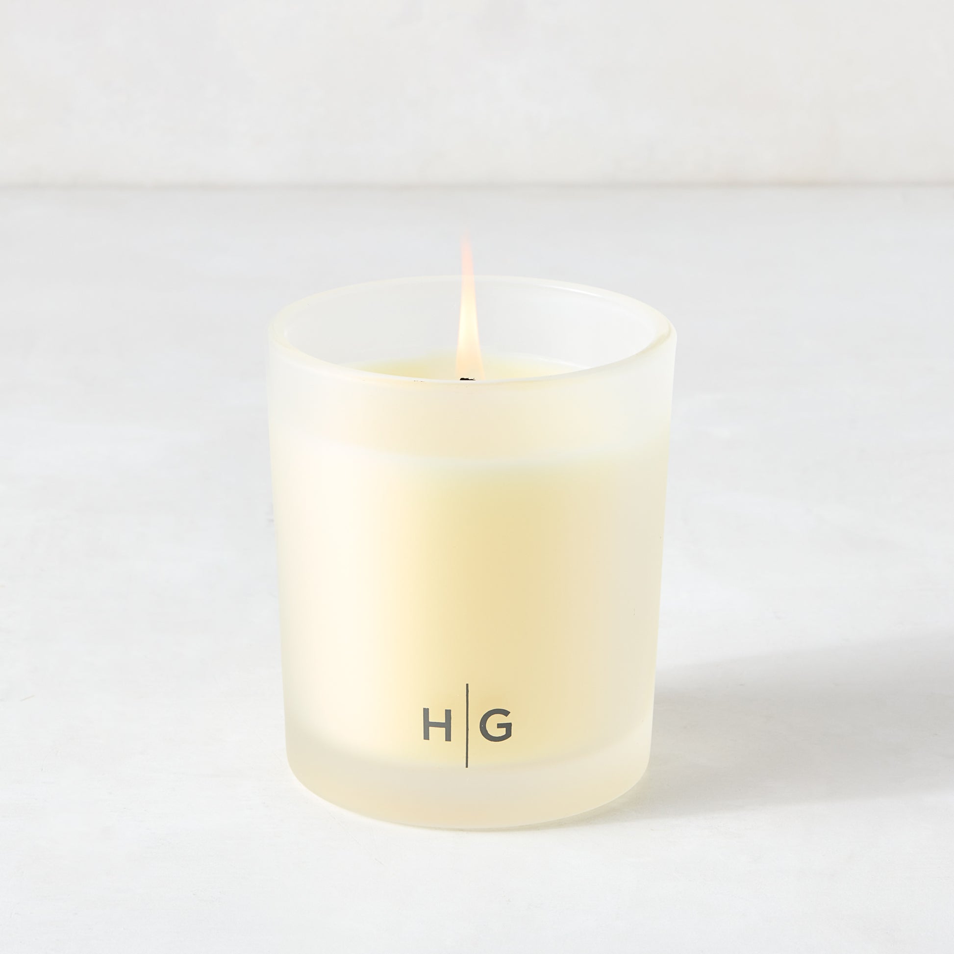 Hudson Grace Palm Beach scented candle in a frosted glass vessel with HG logo, burning.