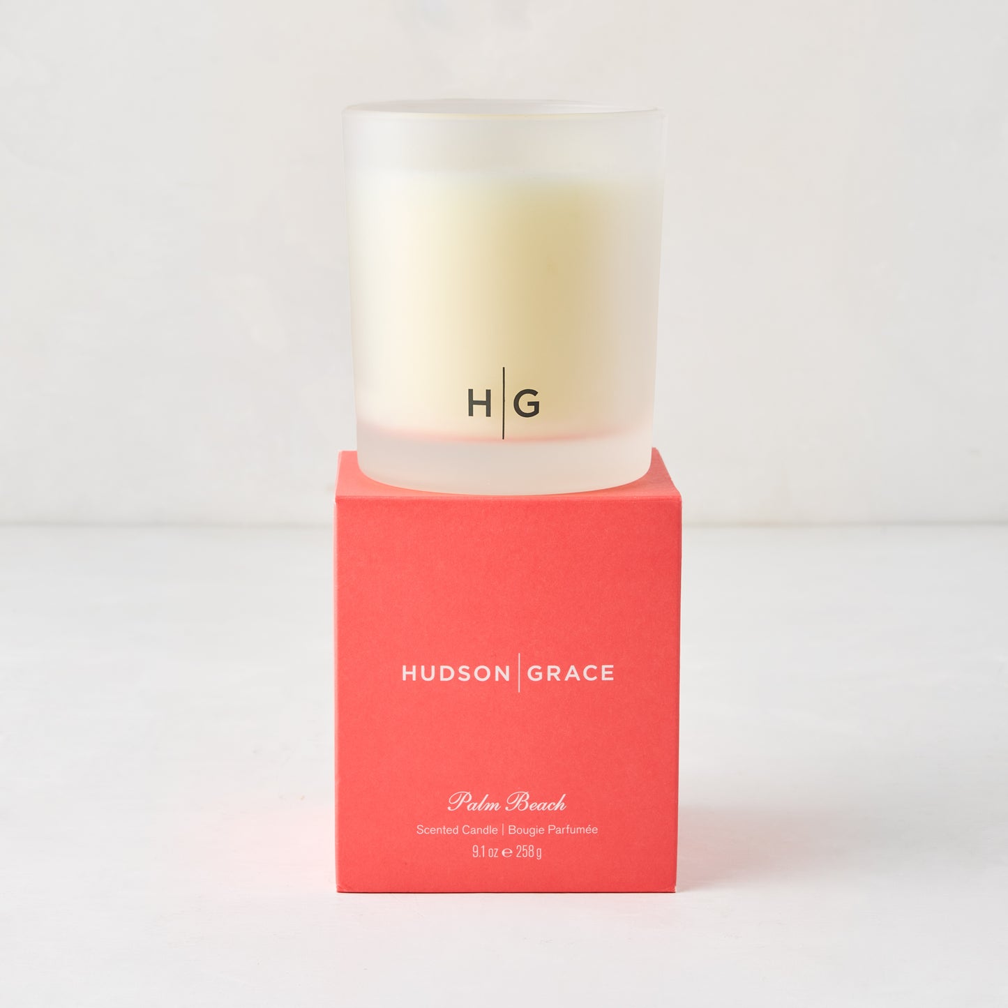 Hudson Grace Palm Beach scented candle in a frosted glass vessel with HG logo, on a coral red box.