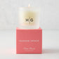 Hudson Grace Palm Beach Scented Votive Candle in a frosted glass vessel with HG logo, on a coral box.