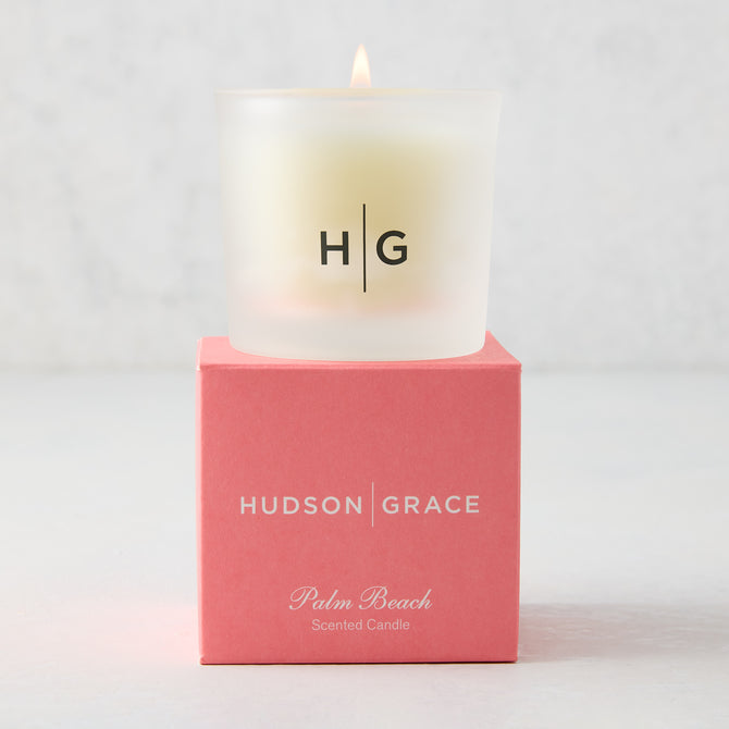 Hudson Grace Palm Beach Scented Votive Candle in a frosted glass vessel with HG logo, on a coral box.