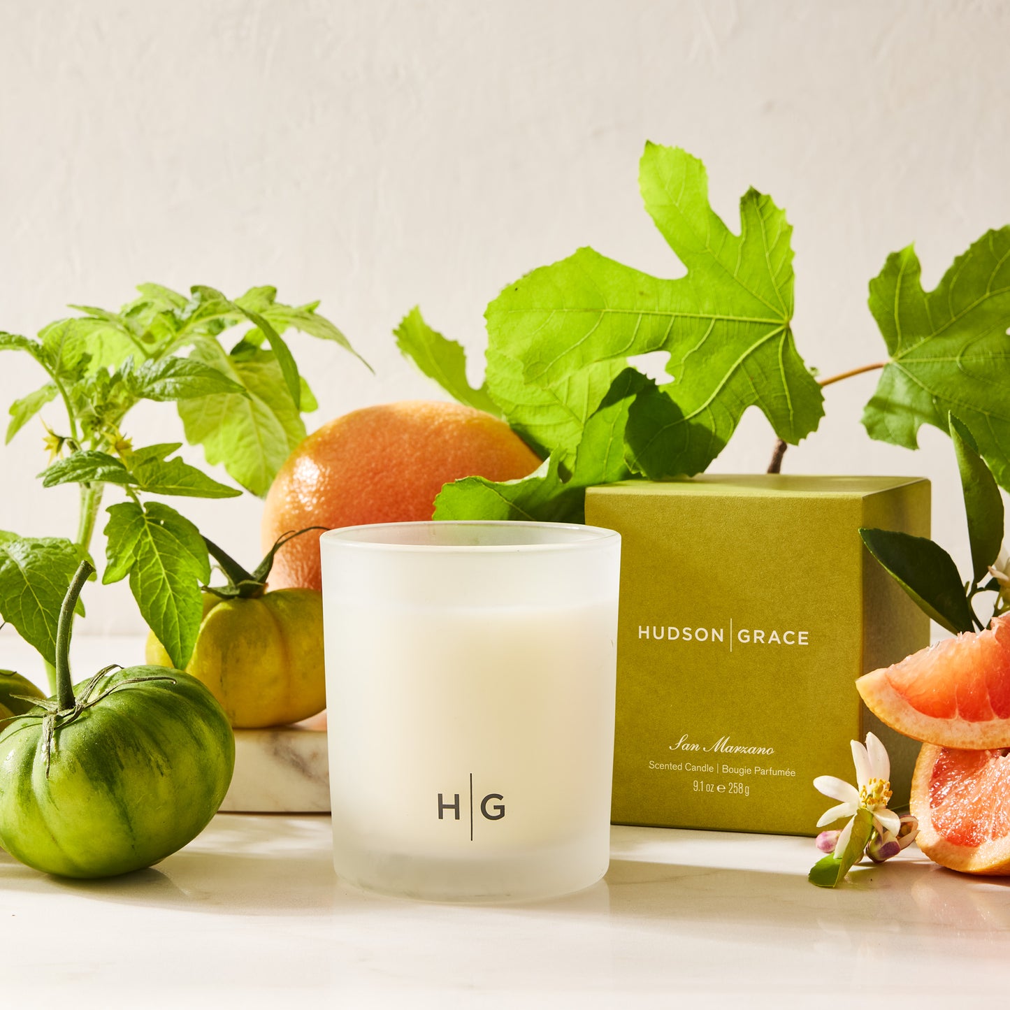 Hudson Grace San Marzano Votive candle in a frosted glass vessel with green tomatoes and grapefruit.