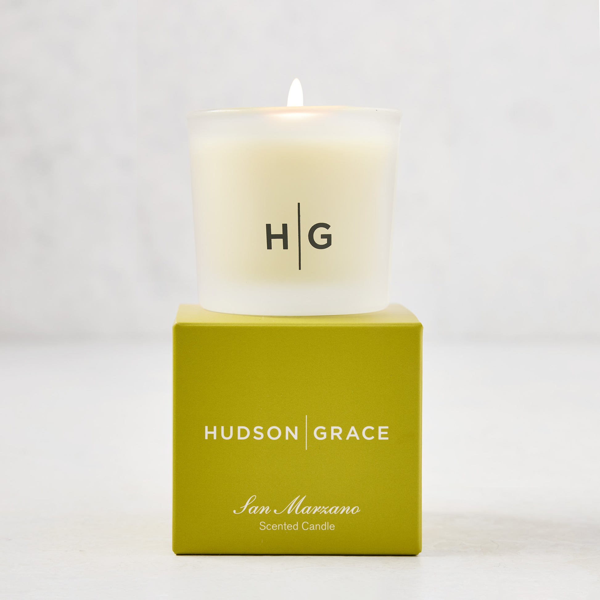 Hudson Grace San Marzano Votive candle in a frosted glass vessel with "HG" logo, atop a green box.
