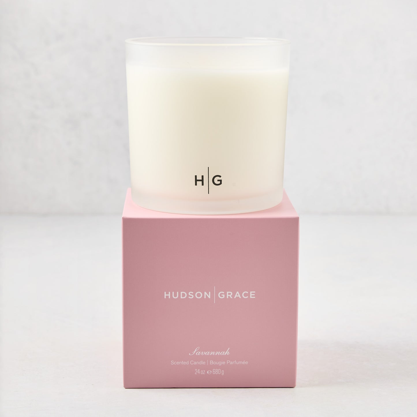 Hudson Grace Savannah 3-wick candle in a frosted glass vessel with HG logo, on a pink gift box.