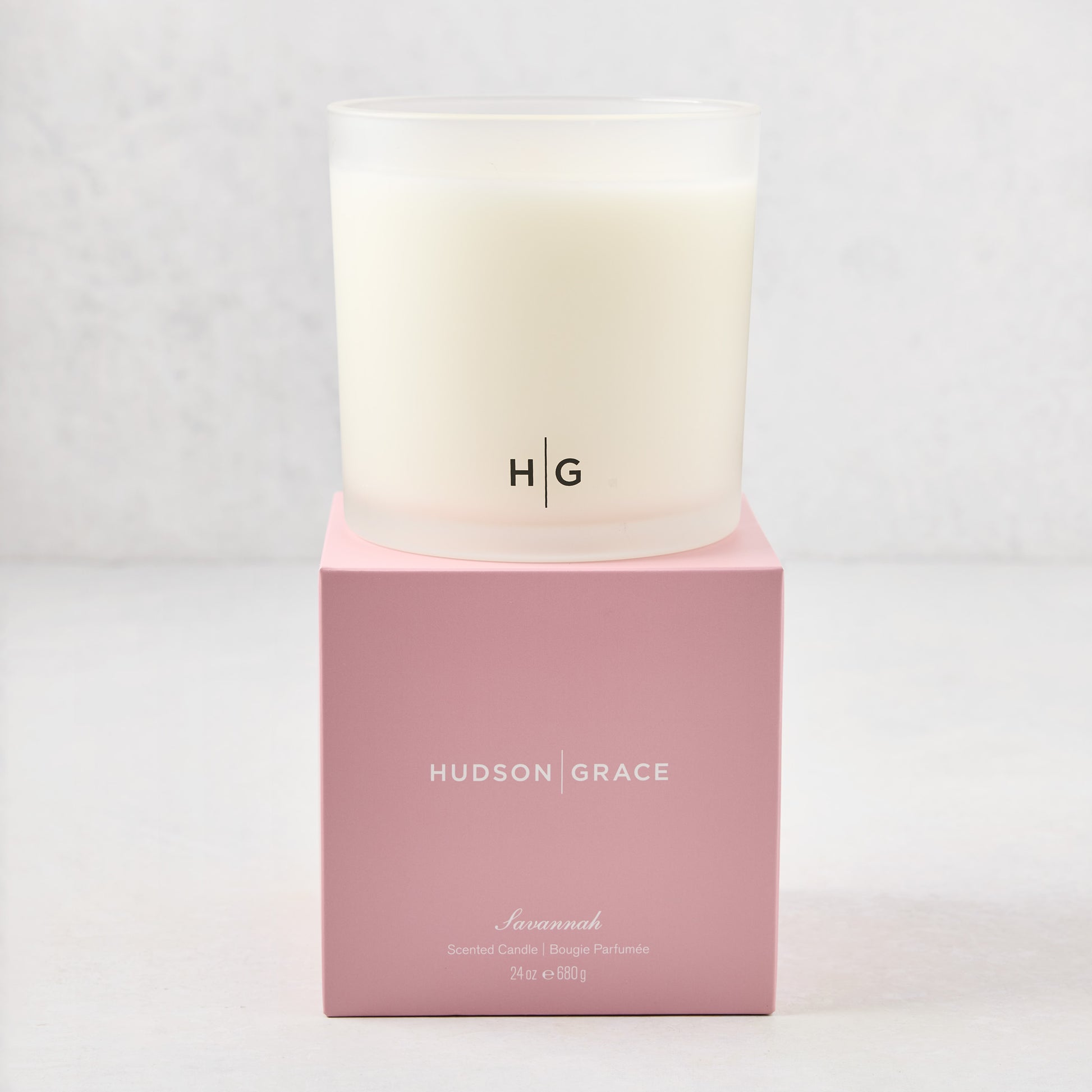 Hudson Grace Savannah 3-wick candle in a frosted glass vessel with HG logo, on a pink gift box.