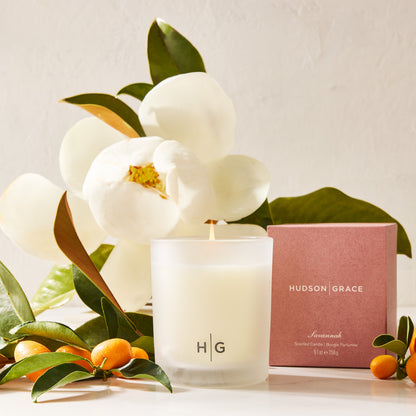 Hudson Grace Savannah Scented Candle in a frosted glass vessel with a pink box, magnolia, and kumquats.