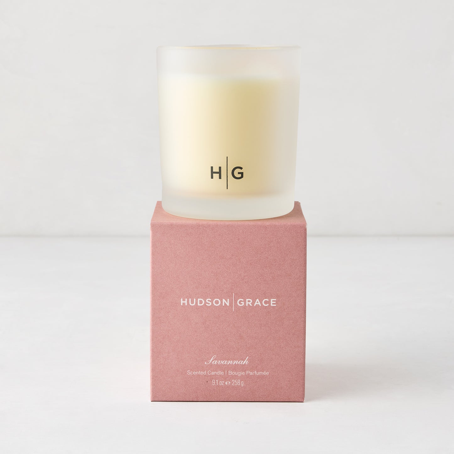 Hudson Grace Savannah scented candle in a frosted glass vessel with HG logo, on a pink box.