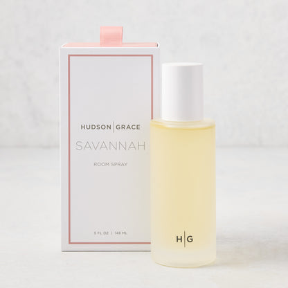 Hudson Grace Savannah Scented Room Spray: 5.08 oz clear glass bottle with white cap next to a white box with pink ribbon.