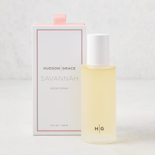 Hudson Grace Savannah Scented Room Spray: 5.08 oz clear glass bottle with white cap next to a white box with pink ribbon.
