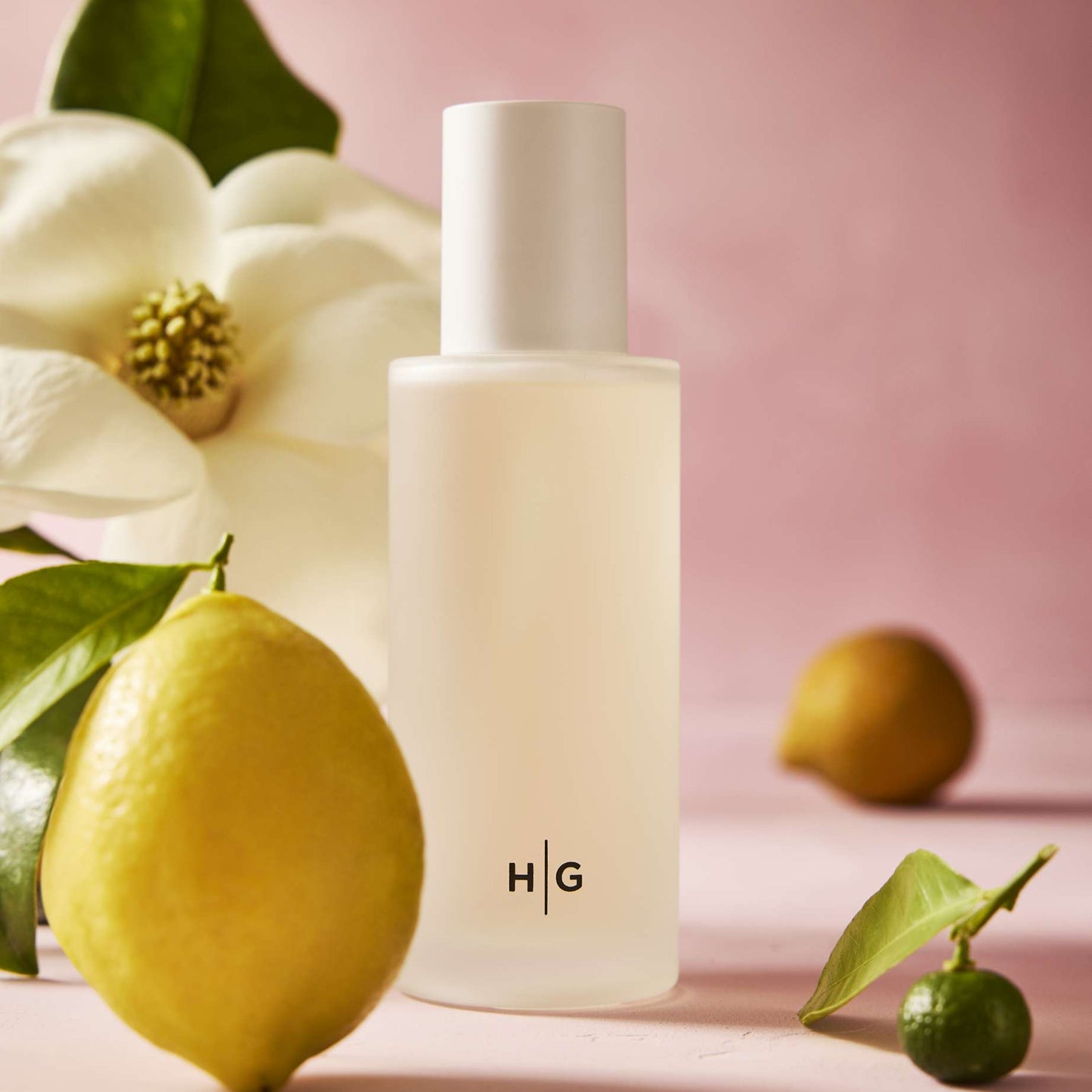 Hudson Grace Savannah scented votive candle in a frosted glass vessel with HG logo, surrounded by magnolia, lemon, and lime.