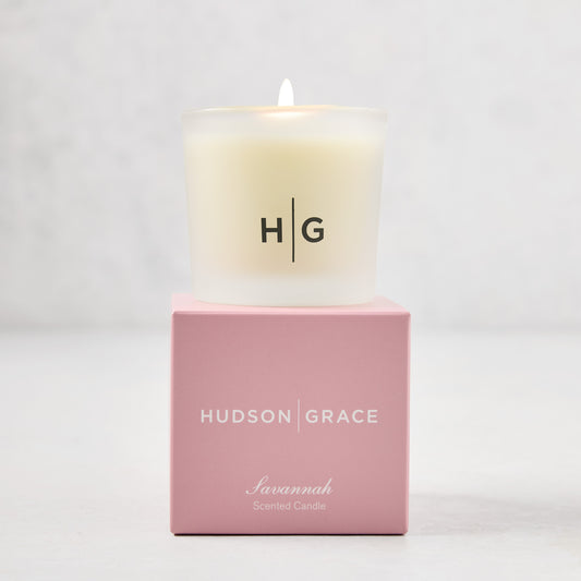 Hudson Grace Savannah Votive Scented Candle in frosted glass vessel with HG logo, on a pink gift box.