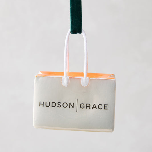 Hudson Grace shopping bag Christmas ornament, white with orange tissue, black logo, green ribbon.