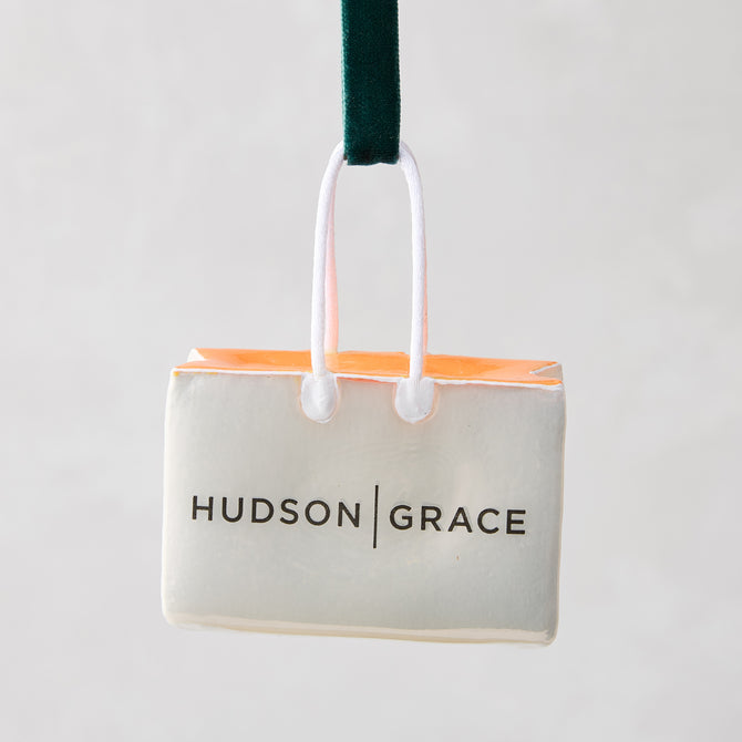 Hudson Grace shopping bag Christmas ornament, white with orange tissue, black logo, green ribbon.
