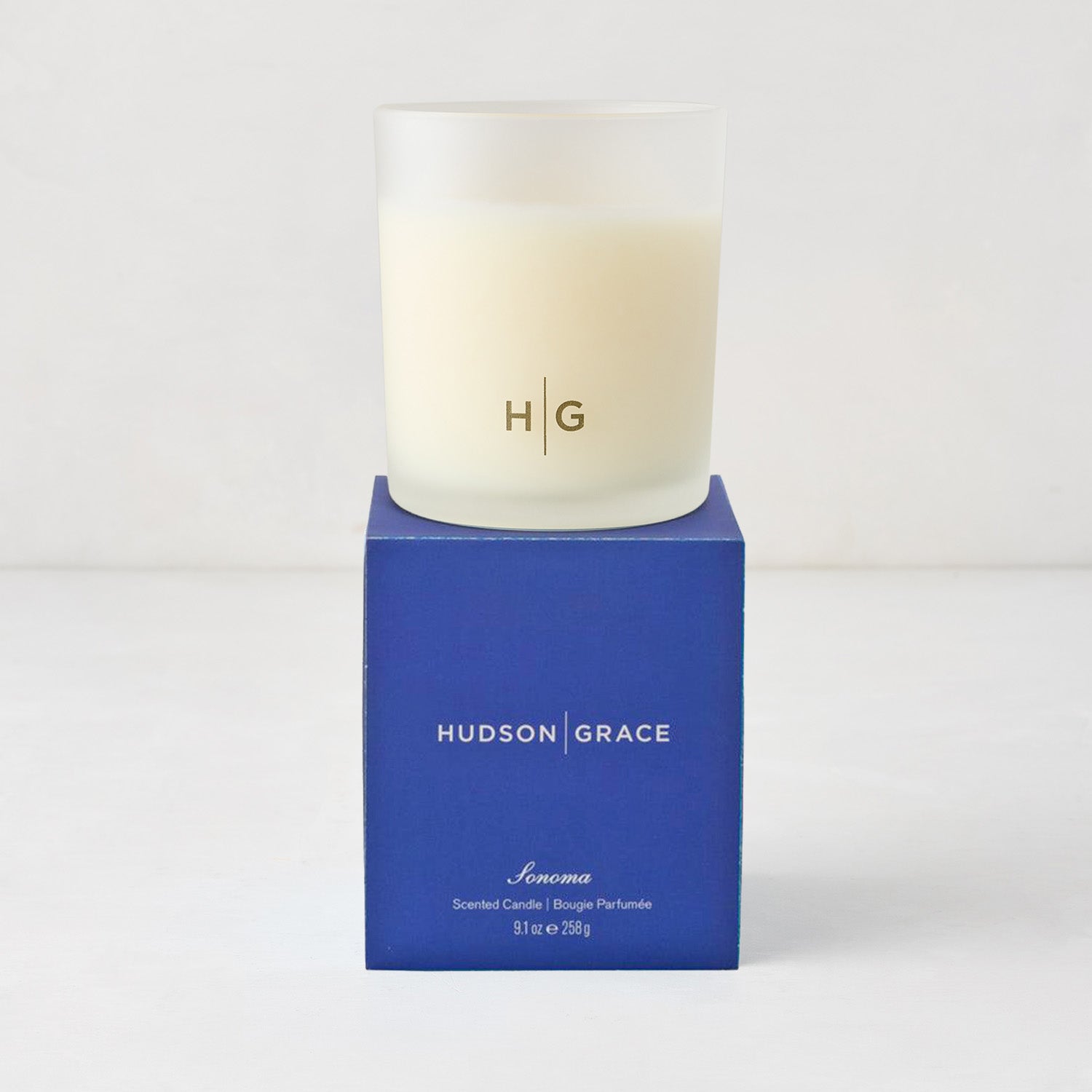 Hudson Grace Sonoma Scented Candle in a frosted glass vessel with "HG" logo, on a blue gift box.