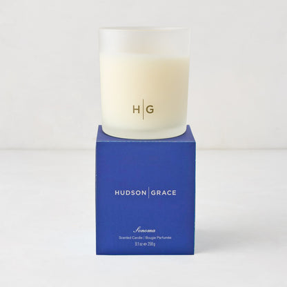 Hudson Grace Sonoma Scented Candle in a frosted glass vessel with "HG" logo, on a blue gift box.