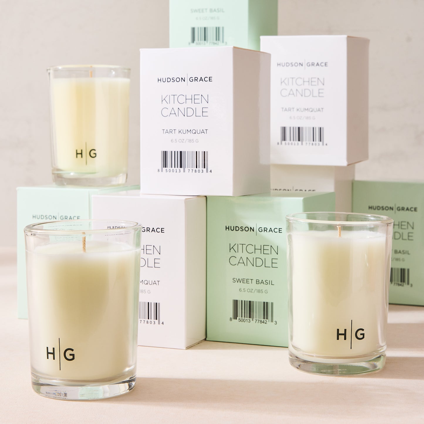 Hudson Grace Tart Kumquat Kitchen Candle in a clear glass jar with white wax, surrounded by white and mint green boxes.