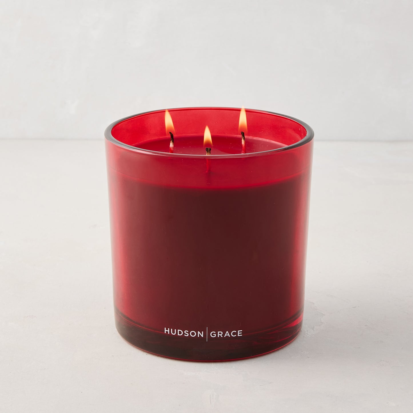 Hudson Grace Winter Scented 3-Wick Candle in a red glass vessel with red wax, lit.
