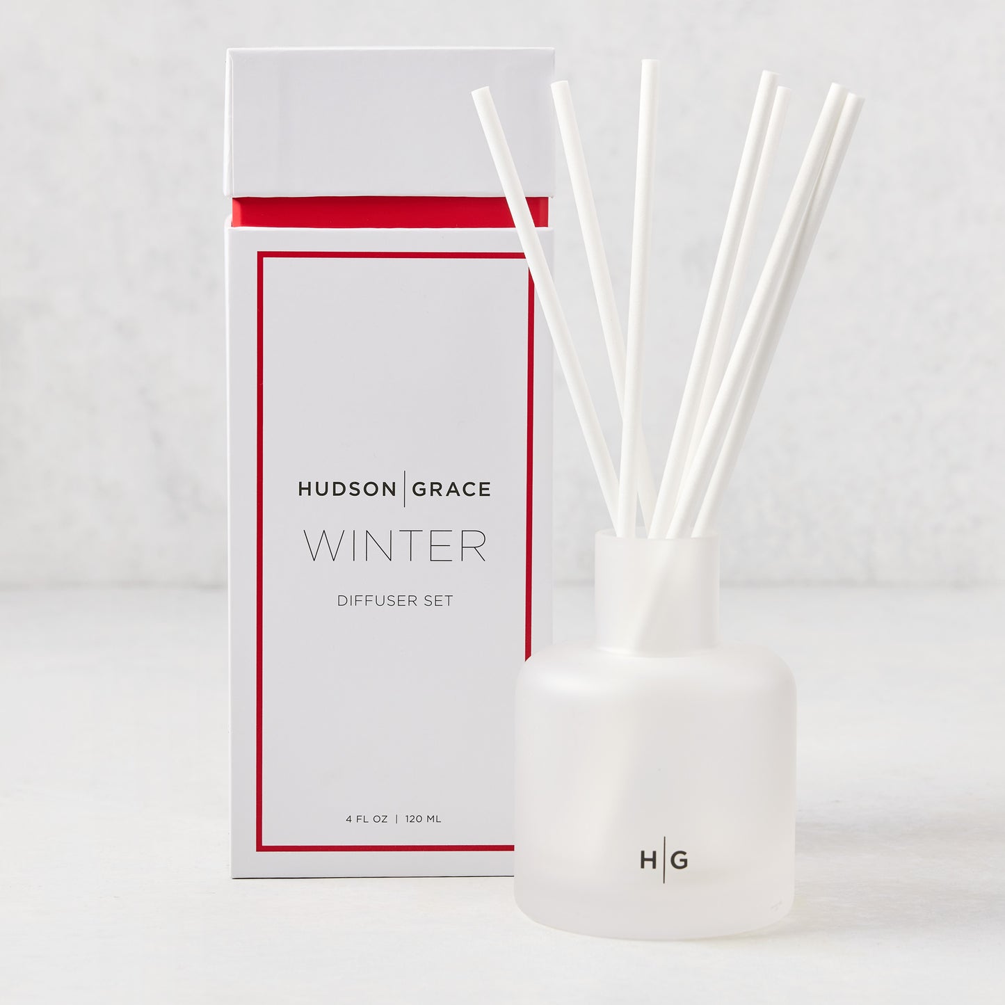 Hudson Grace Winter Scented Reed Diffuser set with a white frosted glass vessel, white reeds, and white box with red trim.