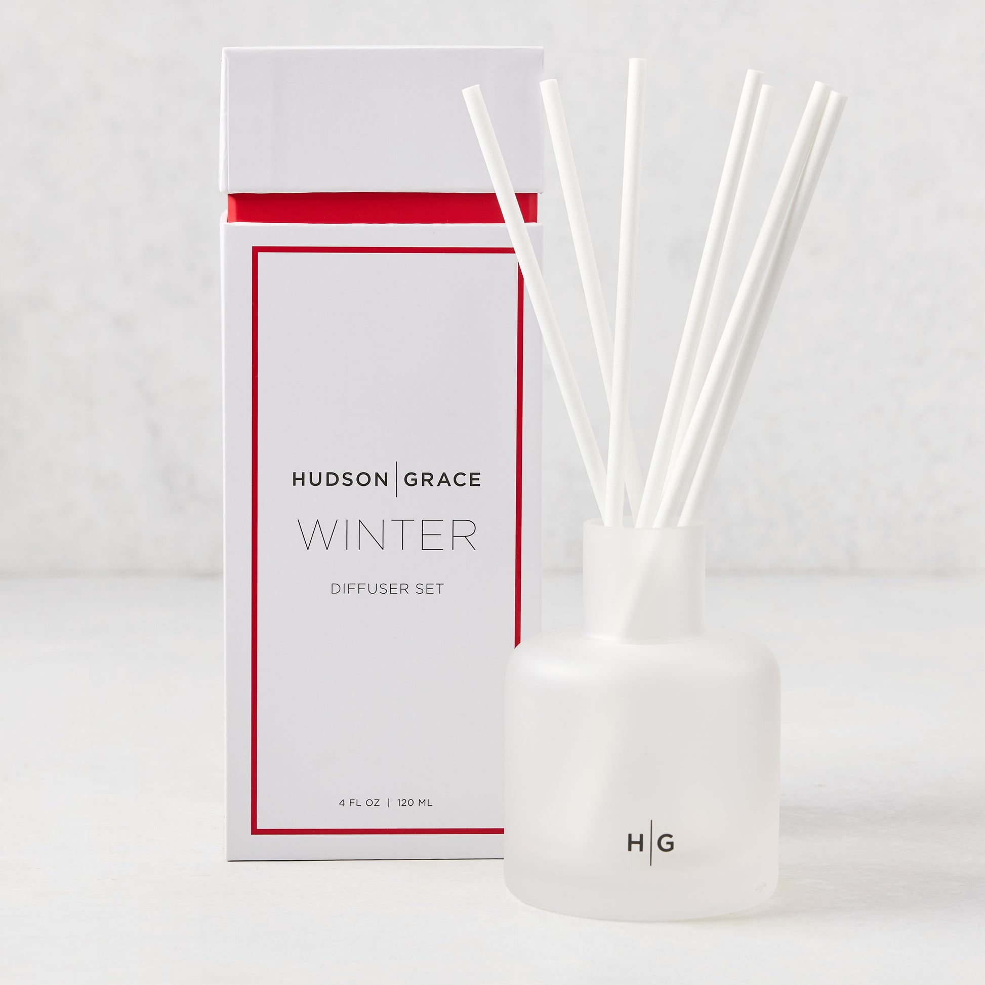 Hudson Grace Winter Scented Reed Diffuser set with a white frosted glass vessel, white reeds, and white box with red trim.