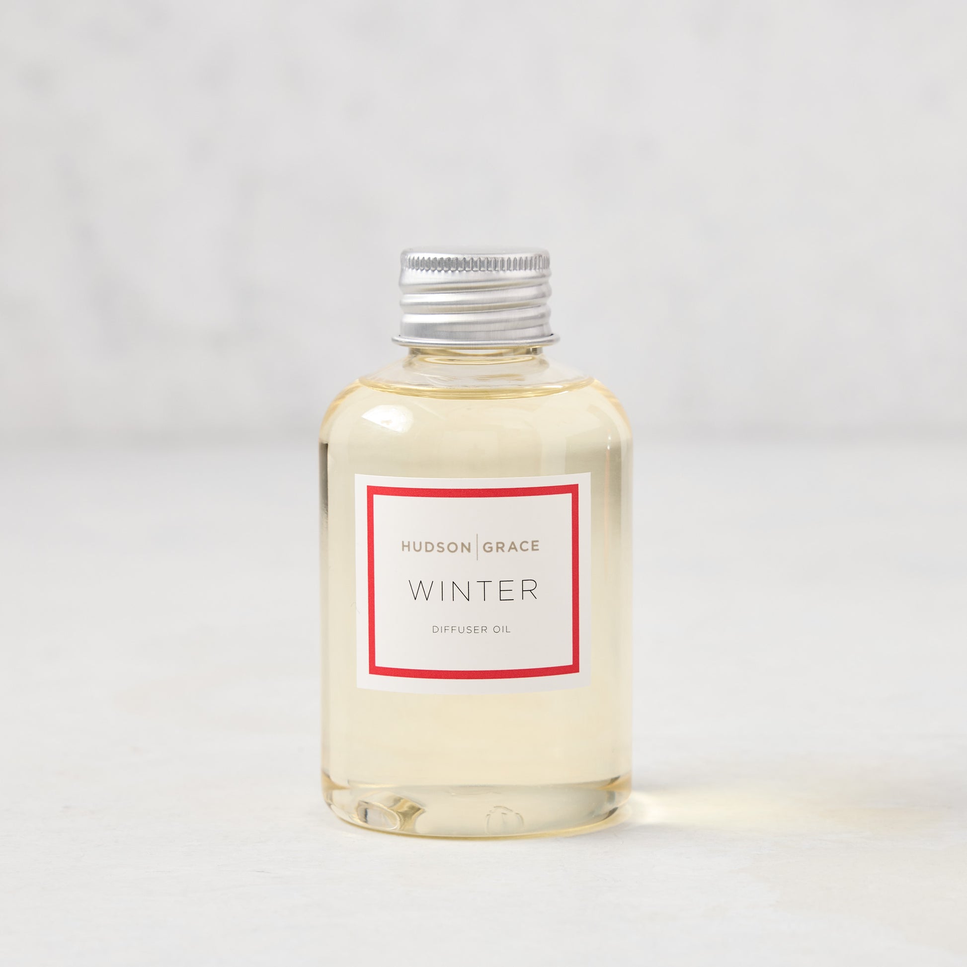 Hudson Grace Winter Scented Reed Diffuser oil bottle, clear glass with silver cap and white label.