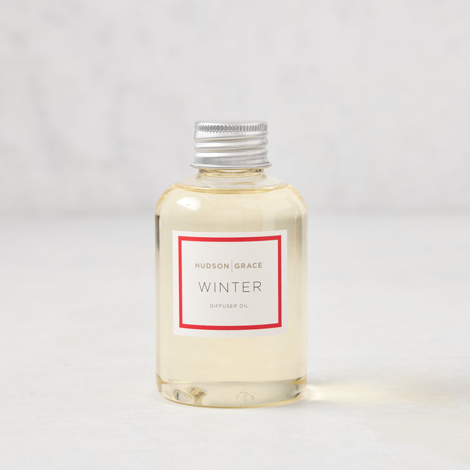 Hudson Grace Winter scented reed diffuser oil refill, clear glass bottle with silver cap, white label.