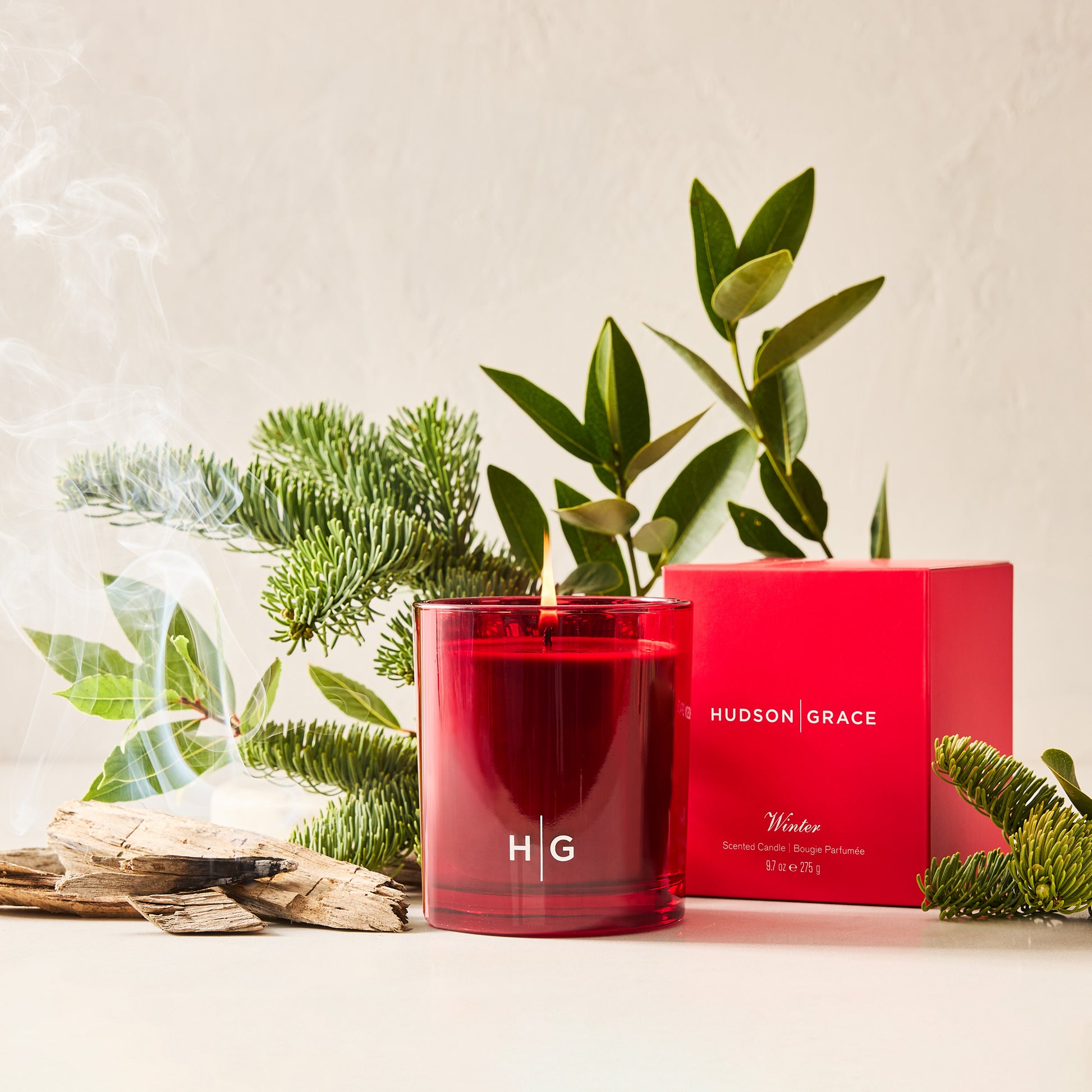 Hudson Grace Winter Scented Candle in a red glass jar with a red box, pine, and wood.