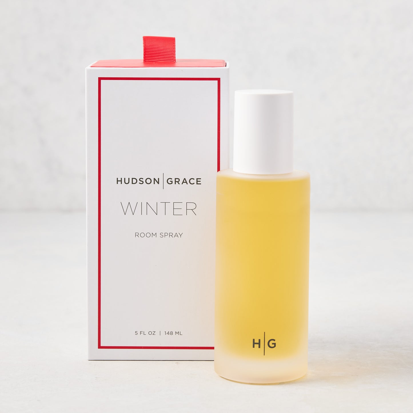 Hudson Grace Winter Scented Room Spray: clear glass bottle with yellow liquid, white cap, next to white box with red trim.