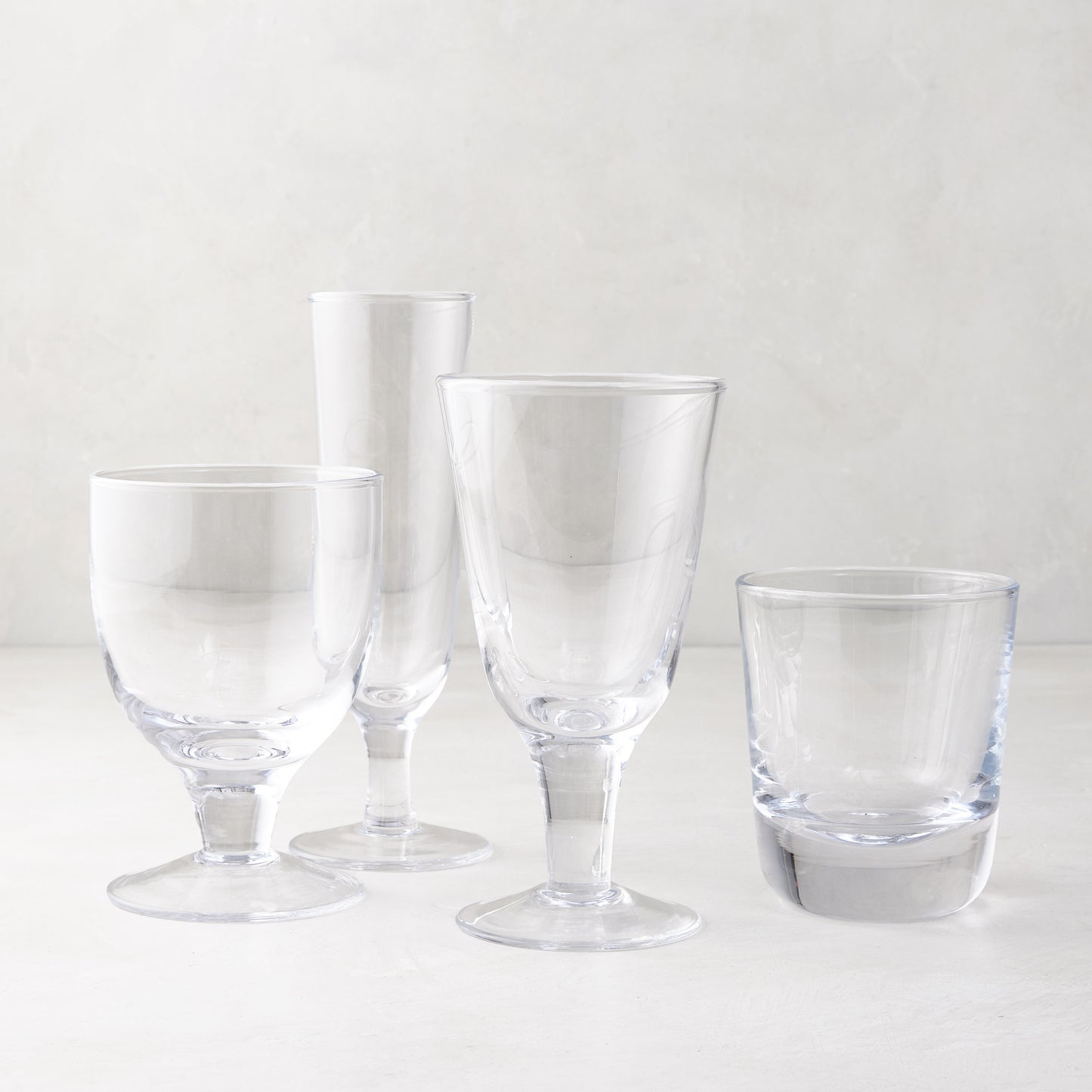 Clear glass stemless and stemmed glasses, including a chunky Hudson glass, on a white surface.