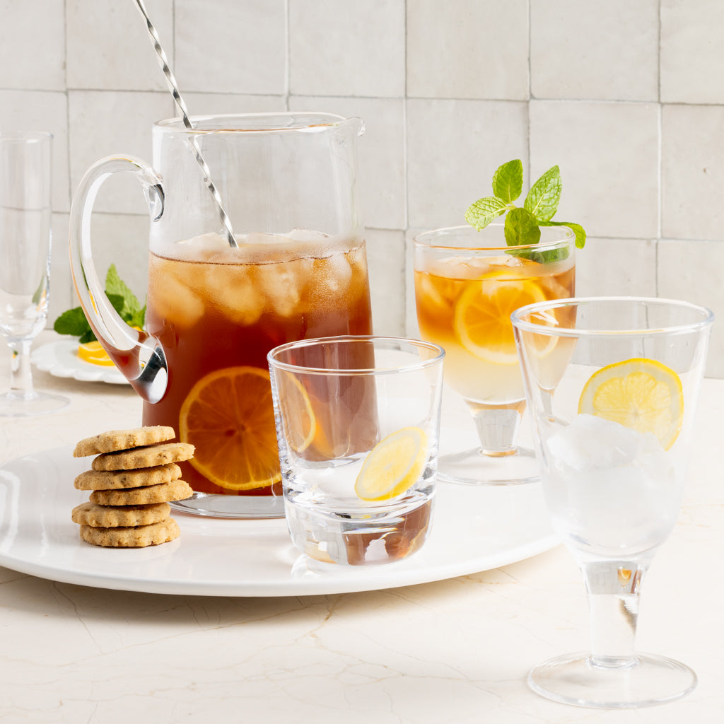 Clear Hudson wine glass with a chunky base, alongside other glassware, drinks, and cookies on a white tray.