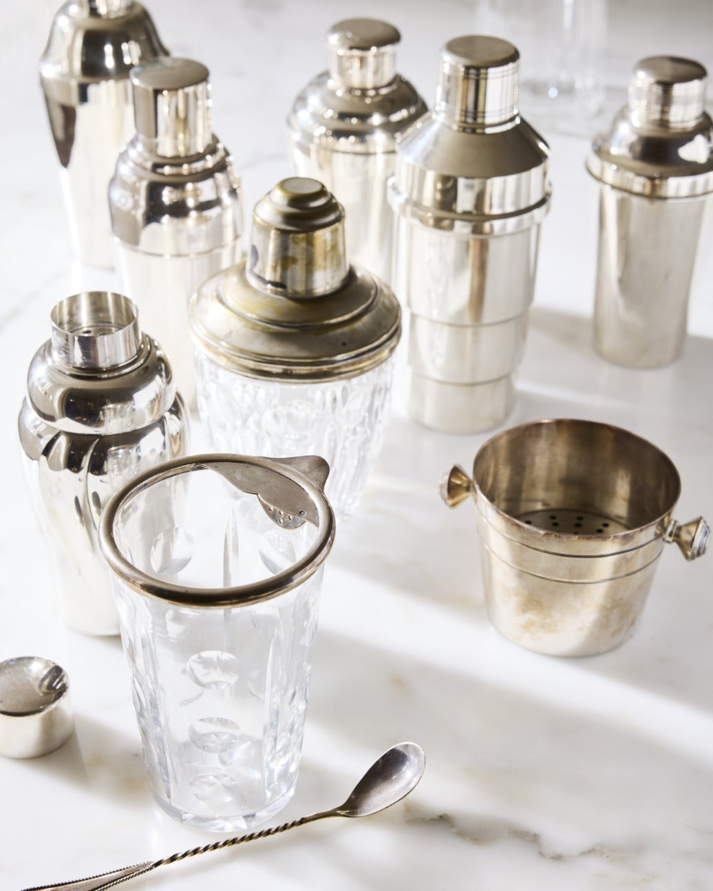 Collection of vintage silver cocktail shakers and bar tools on a marble surface
