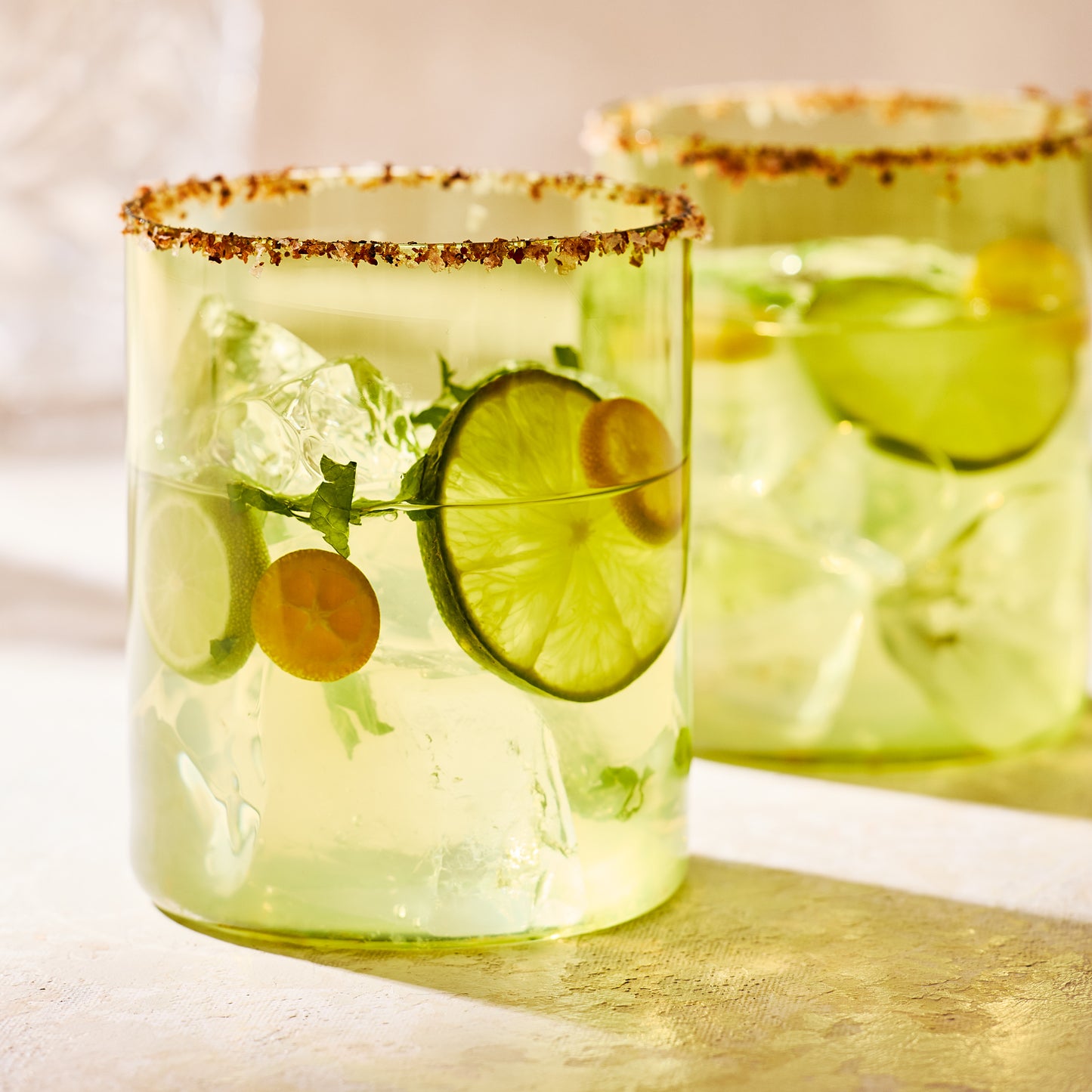 Hugo Aloe Green Double Old Fashioned Glass with a rimmed cocktail, lime slices, and ice.