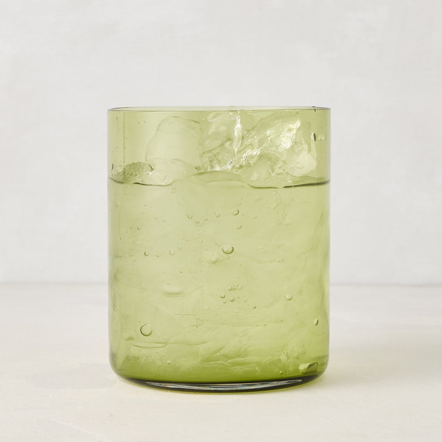 Hugo Aloe Green Double Old Fashioned Glass, filled with ice and a clear drink. Handmade glass, 3.25"Dia x 4"H.