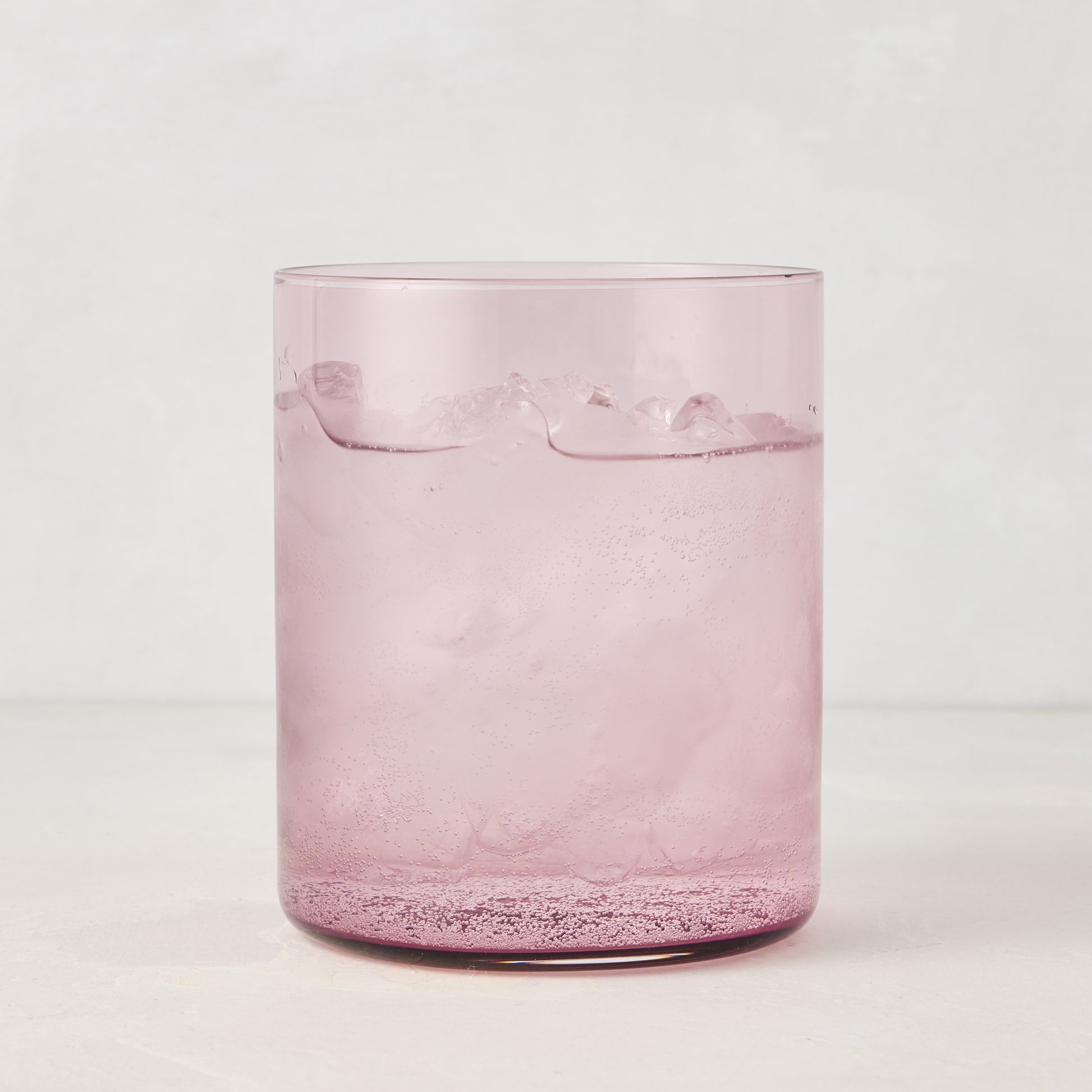 Hugo Fig Double Old Fashioned Glass, a sleek, sturdy pink glass with ice and a sparkling drink.