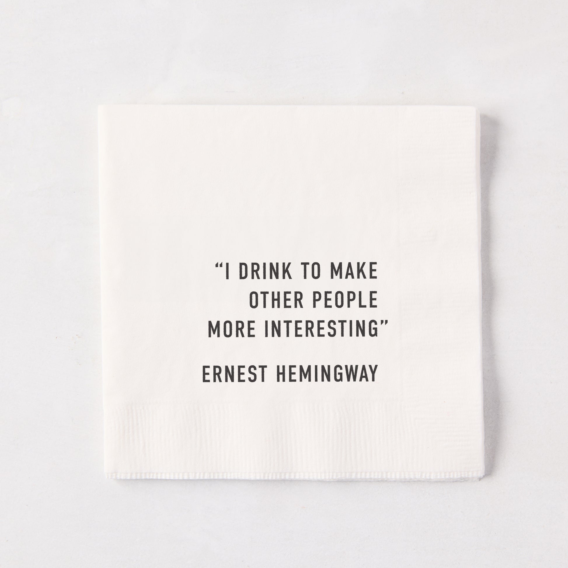White 5.5-inch square 3-ply paper cocktail napkin with black text reading I Drink To Make Other People Interesting.