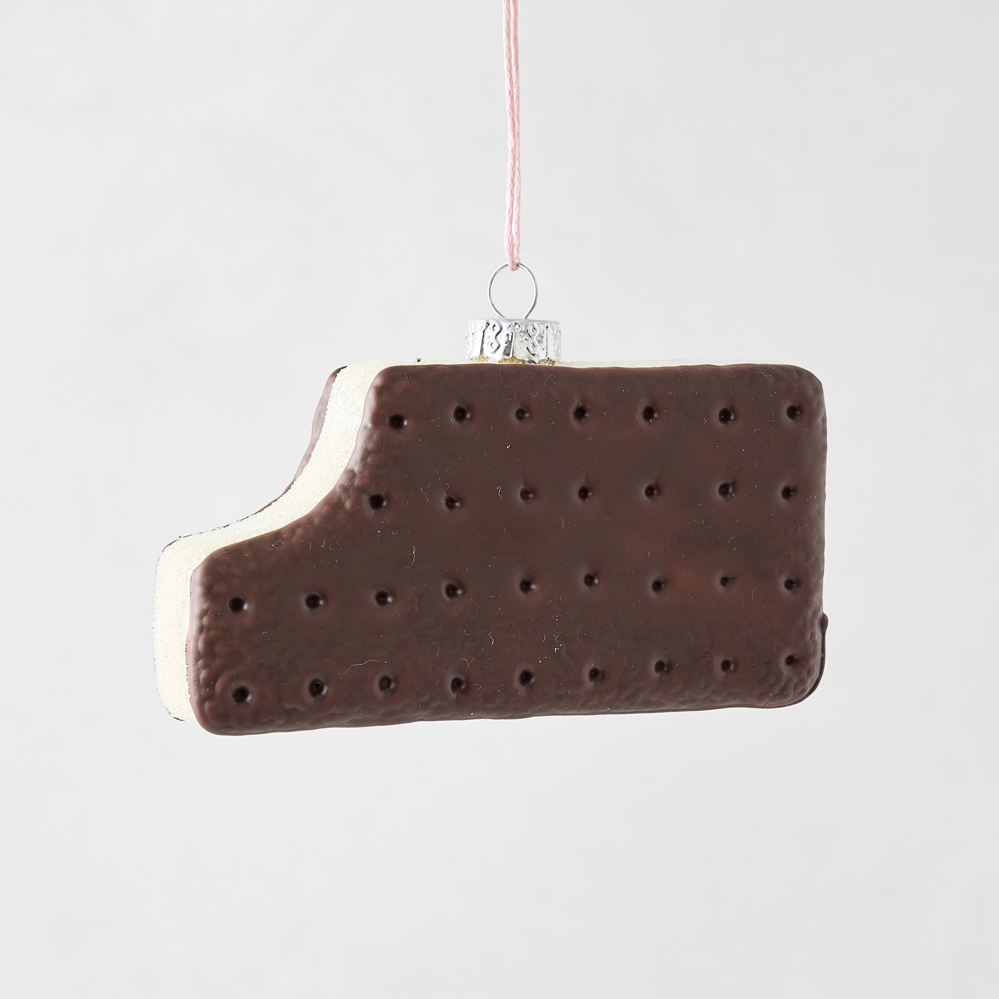 Hand-painted glass and resin ice cream sandwich ornament with a bite taken out, hanging from a pink string.