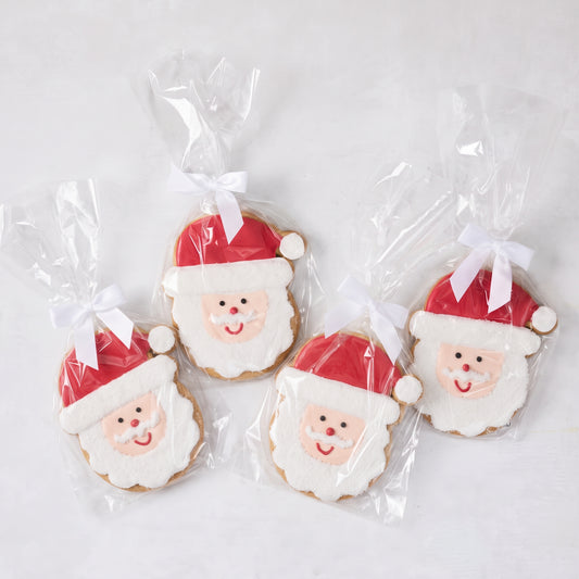 Set of four oversized sugar cookies shaped like Santa Claus, decorated with red and white icing, individually wrapped with white bows.